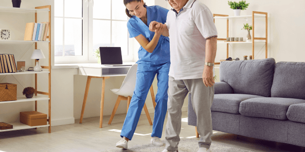 nurse in senior living facility holding elderly patient by hand and helping him walk